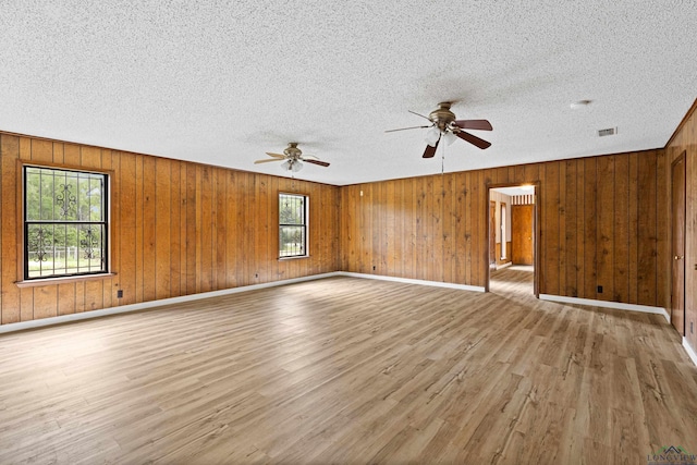 unfurnished room featuring ceiling fan, light hardwood / wood-style flooring, and wooden walls