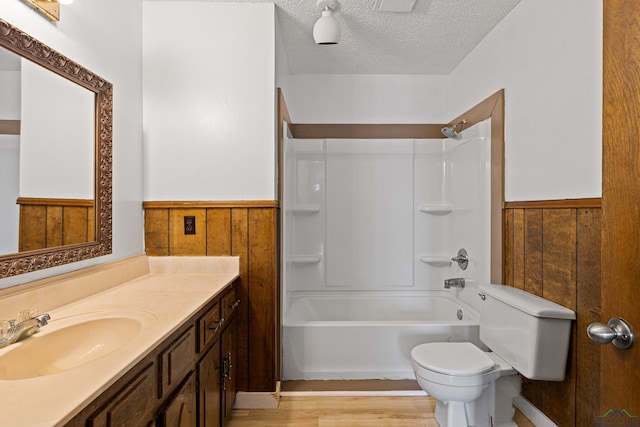 full bathroom with vanity, wood walls, toilet, a textured ceiling, and shower / bathtub combination