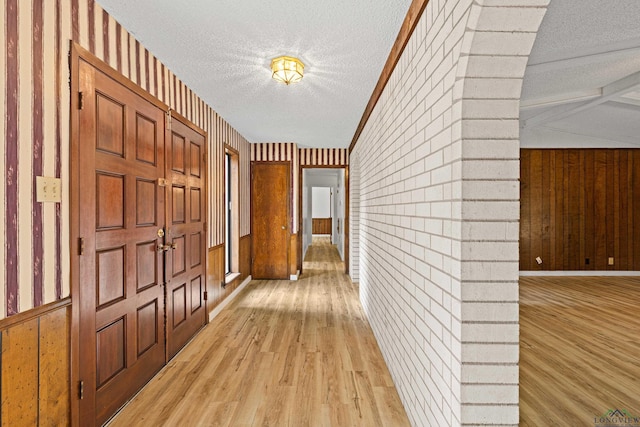 hallway featuring vaulted ceiling, wood walls, light hardwood / wood-style flooring, and a textured ceiling