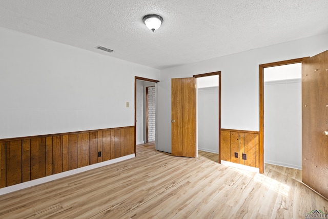 unfurnished bedroom featuring wood walls, light hardwood / wood-style flooring, and a textured ceiling