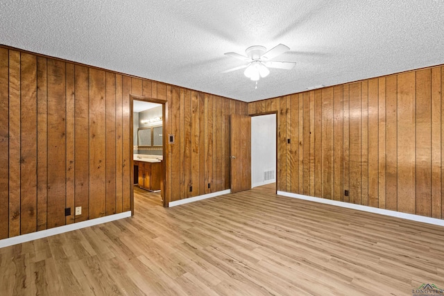 unfurnished bedroom with ceiling fan, ensuite bath, wooden walls, and light hardwood / wood-style flooring