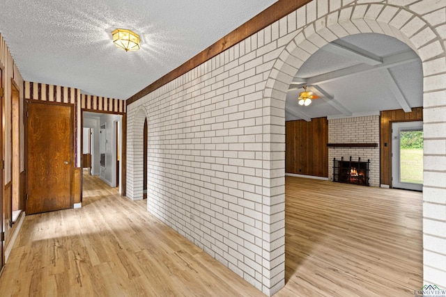 hall with beam ceiling, a textured ceiling, light hardwood / wood-style flooring, and brick wall