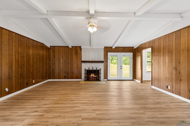 unfurnished living room with french doors, a textured ceiling, ceiling fan, a fireplace, and vaulted ceiling with beams