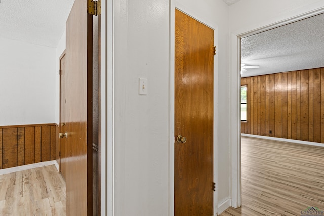 hallway with wood walls, light hardwood / wood-style flooring, and a textured ceiling