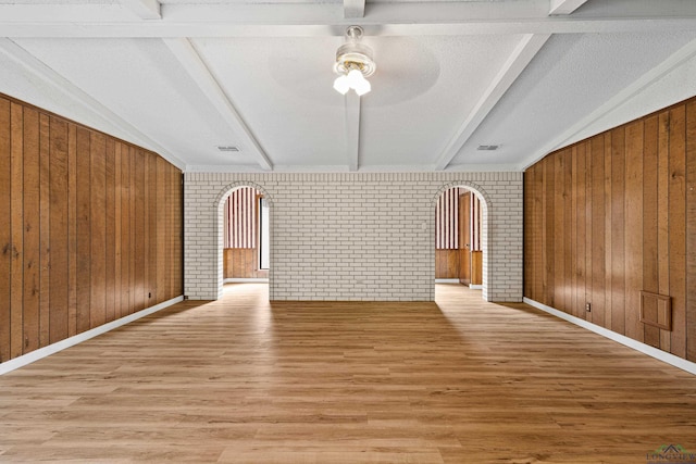 unfurnished living room featuring vaulted ceiling with beams, ceiling fan, wood walls, and brick wall