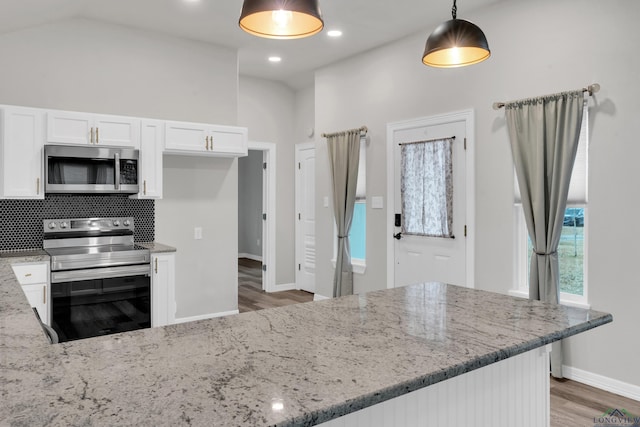 kitchen featuring pendant lighting, appliances with stainless steel finishes, white cabinetry, light stone countertops, and vaulted ceiling