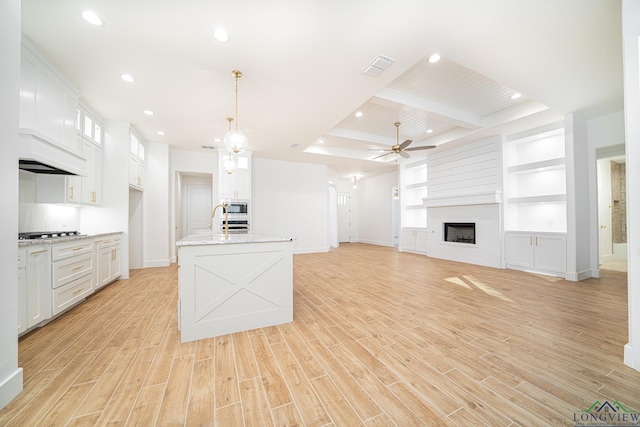 kitchen featuring built in shelves, ceiling fan, light stone counters, pendant lighting, and white cabinets