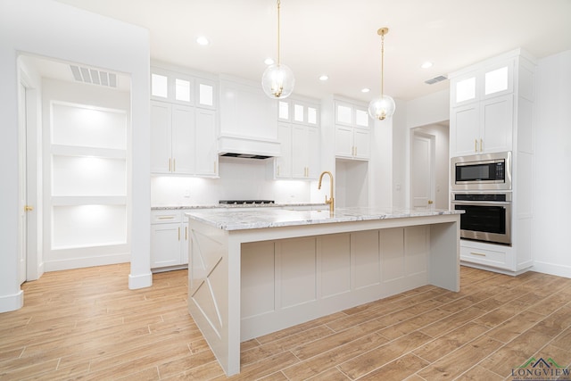 kitchen with white cabinets, appliances with stainless steel finishes, a center island with sink, and hanging light fixtures