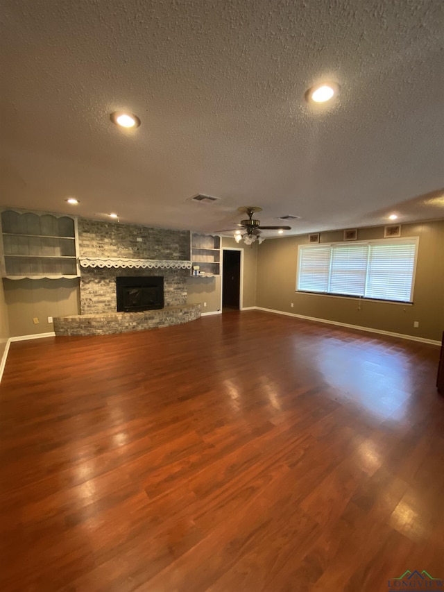 unfurnished living room featuring ceiling fan, hardwood / wood-style floors, a fireplace, a textured ceiling, and built in shelves