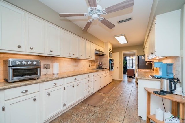 kitchen featuring decorative backsplash, white cabinets, visible vents, and a sink