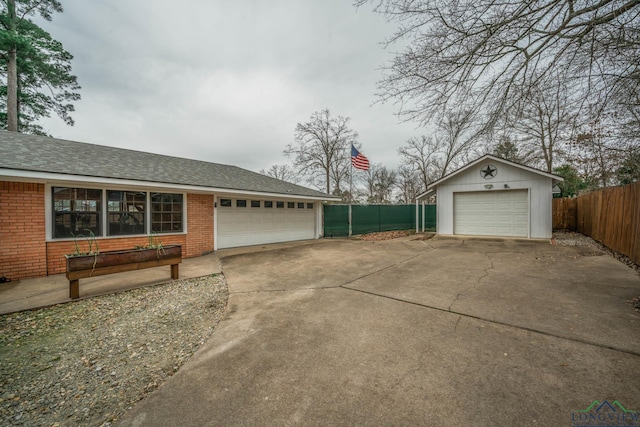 view of side of home with brick siding, a shingled roof, fence, a garage, and an outbuilding