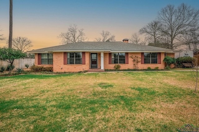 ranch-style house featuring brick siding, a chimney, a front lawn, and fence