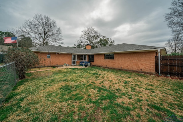 rear view of house featuring brick siding, a fenced backyard, a chimney, and a yard