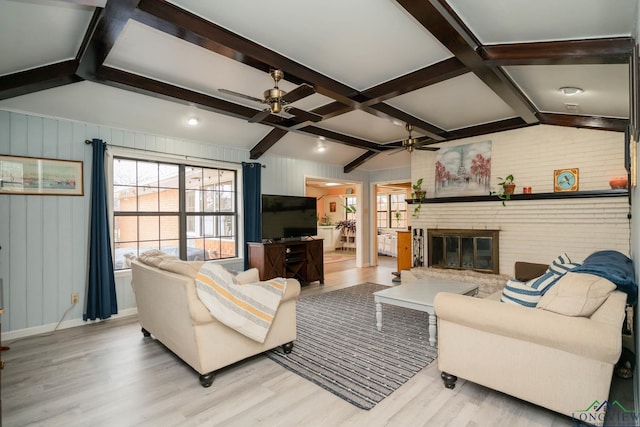 living area featuring a brick fireplace, vaulted ceiling with beams, a ceiling fan, and wood finished floors