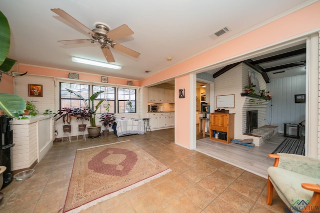 living area featuring visible vents, a brick fireplace, crown molding, and ceiling fan