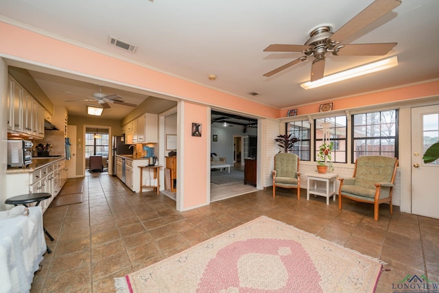 living area with visible vents, ornamental molding, and a ceiling fan