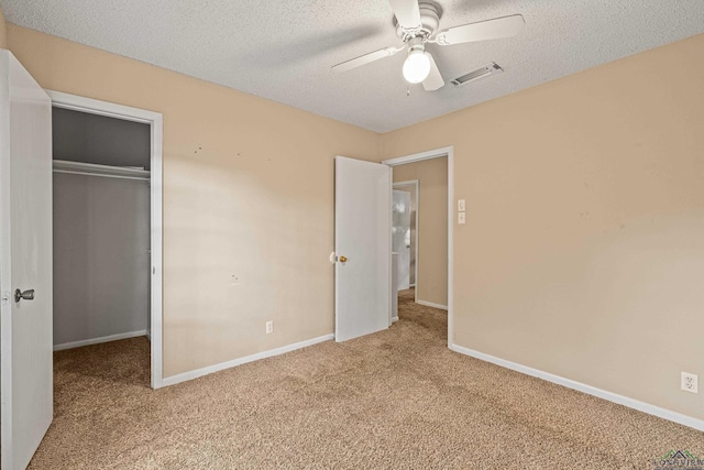 unfurnished bedroom featuring light carpet, a textured ceiling, a closet, and ceiling fan