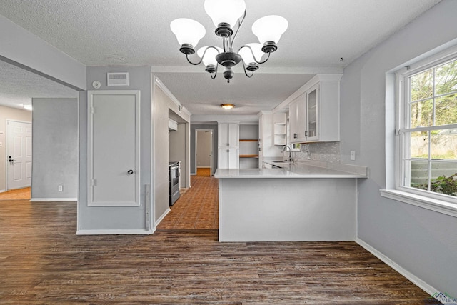 kitchen with kitchen peninsula, stainless steel electric stove, sink, a notable chandelier, and white cabinetry