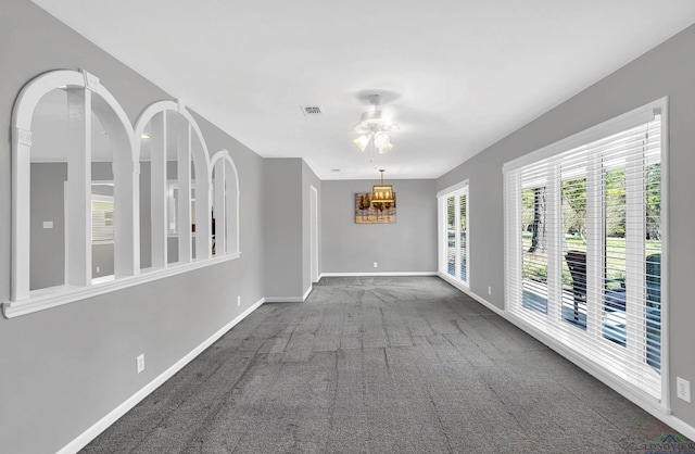 carpeted spare room featuring ceiling fan with notable chandelier