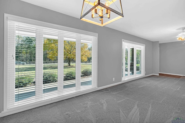 carpeted empty room featuring ceiling fan with notable chandelier