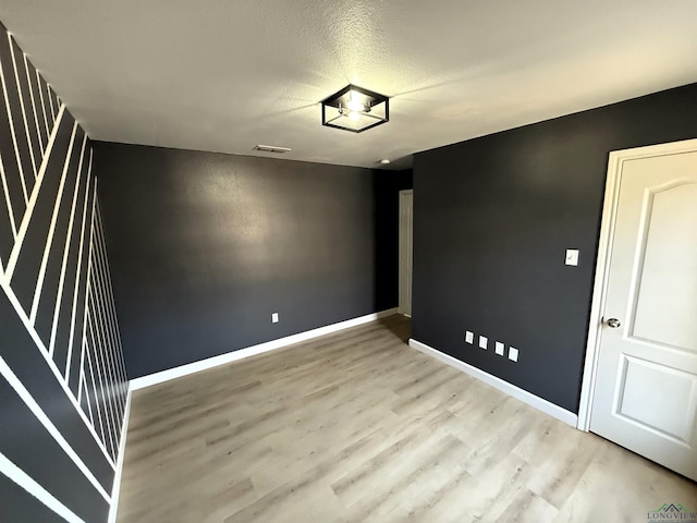 empty room with light wood-type flooring and a textured ceiling