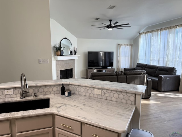 kitchen with vaulted ceiling, ceiling fan, light wood-type flooring, light stone counters, and a tile fireplace