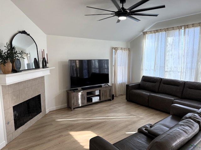 living room featuring light wood-type flooring, ceiling fan, lofted ceiling, and a tiled fireplace