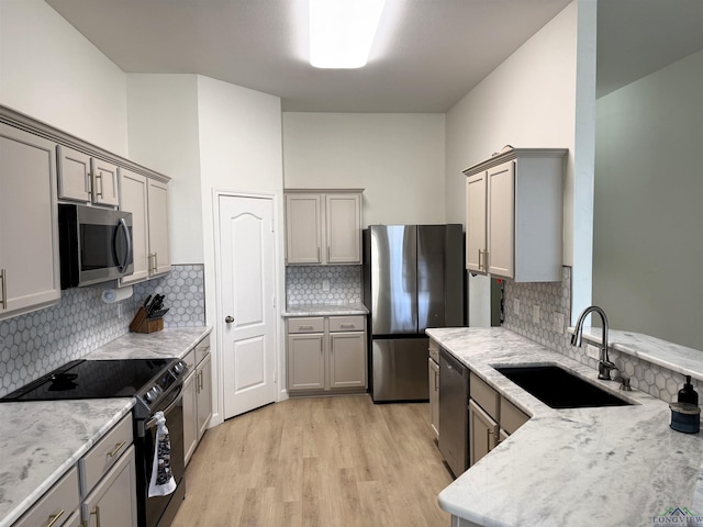 kitchen with decorative backsplash, sink, light hardwood / wood-style flooring, light stone countertops, and stainless steel appliances