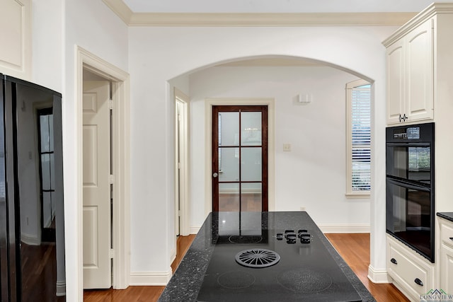 kitchen featuring baseboards, arched walkways, dark wood-style floors, crown molding, and black appliances