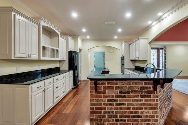 kitchen with dark wood-type flooring, crown molding, a kitchen bar, white cabinets, and black appliances