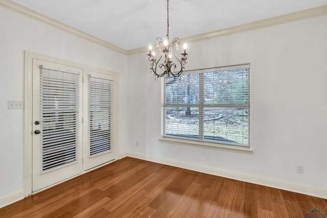 unfurnished dining area with wood finished floors, a notable chandelier, ornamental molding, and baseboards