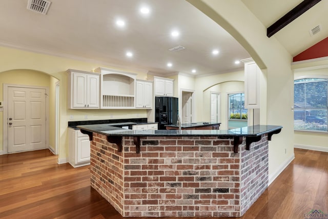 kitchen with dark wood-type flooring, vaulted ceiling with beams, black fridge, a breakfast bar area, and white cabinets