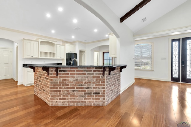 kitchen with black fridge, open shelves, dark countertops, a kitchen bar, and vaulted ceiling with beams