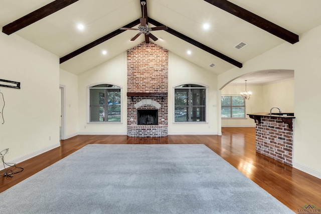 living room with high vaulted ceiling, dark wood-type flooring, ceiling fan with notable chandelier, and a brick fireplace