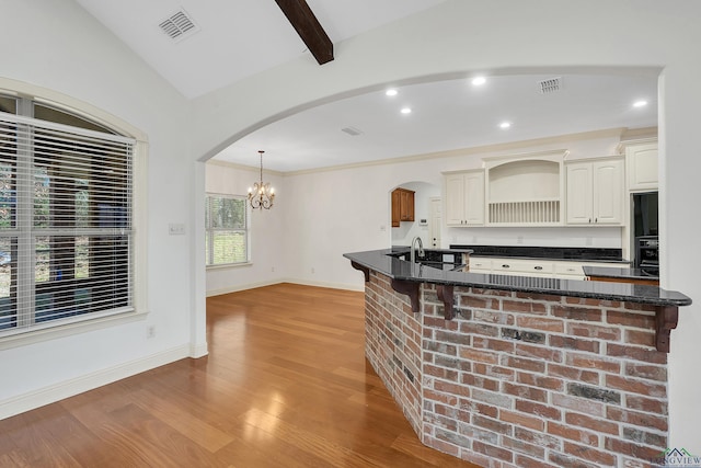 kitchen featuring visible vents, baseboards, a chandelier, light wood finished floors, and vaulted ceiling with beams