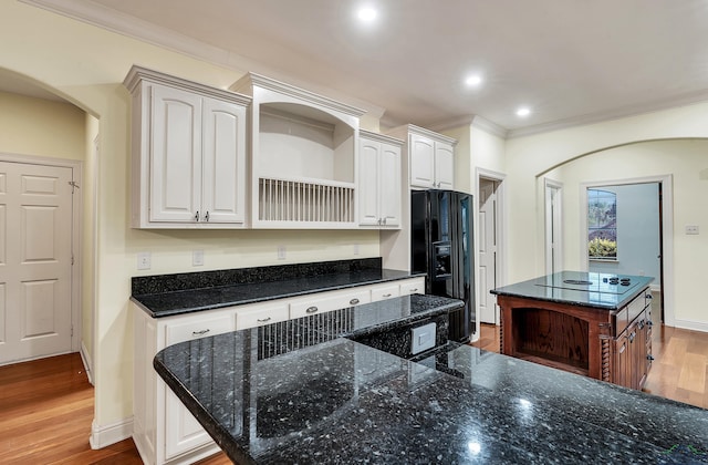 kitchen featuring white cabinets, black fridge with ice dispenser, a kitchen island, and dark stone counters