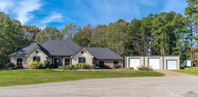 french country home featuring a front yard, stone siding, a garage, and an outbuilding