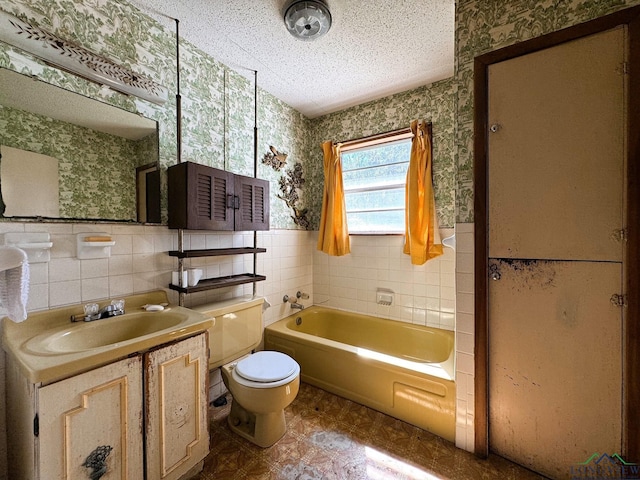 bathroom featuring tile walls, vanity, a washtub, toilet, and a textured ceiling