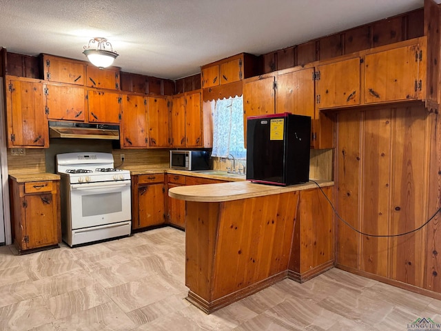 kitchen featuring sink, white gas stove, a textured ceiling, black refrigerator, and kitchen peninsula