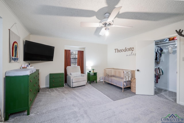 bedroom with a textured ceiling, light carpet, a closet, a crib, and ceiling fan