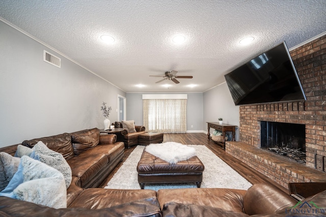 living room with ceiling fan, a brick fireplace, crown molding, hardwood / wood-style flooring, and a textured ceiling