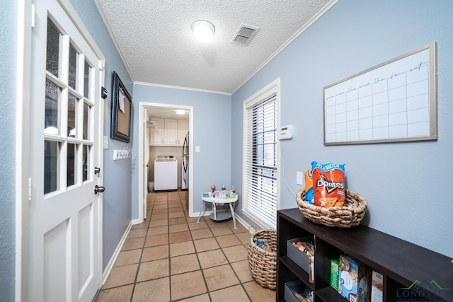 doorway to outside with a textured ceiling, light tile patterned floors, crown molding, and washer / clothes dryer