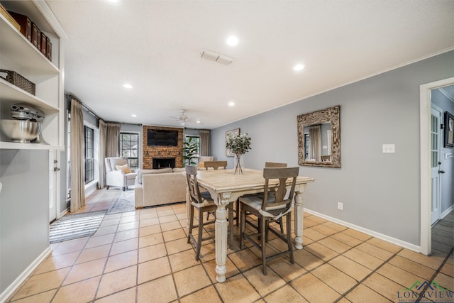 tiled dining area with a brick fireplace, crown molding, and ceiling fan