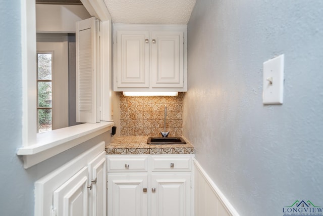 bar featuring a textured ceiling, decorative backsplash, white cabinets, and sink