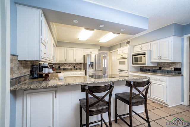 kitchen with white cabinetry, built in microwave, backsplash, and stainless steel fridge