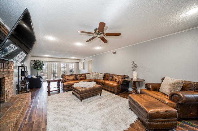 living room featuring ceiling fan, dark hardwood / wood-style floors, a fireplace, french doors, and a textured ceiling