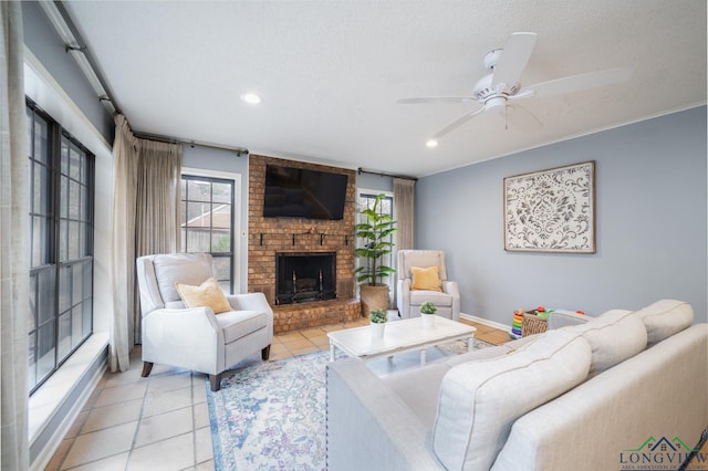 tiled living room with ceiling fan, a brick fireplace, a wealth of natural light, and a textured ceiling