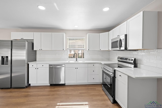 kitchen featuring light countertops, appliances with stainless steel finishes, light wood-style floors, white cabinets, and a sink