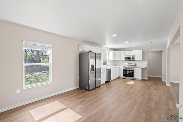 kitchen featuring stainless steel appliances, white cabinetry, light wood-style floors, baseboards, and light countertops