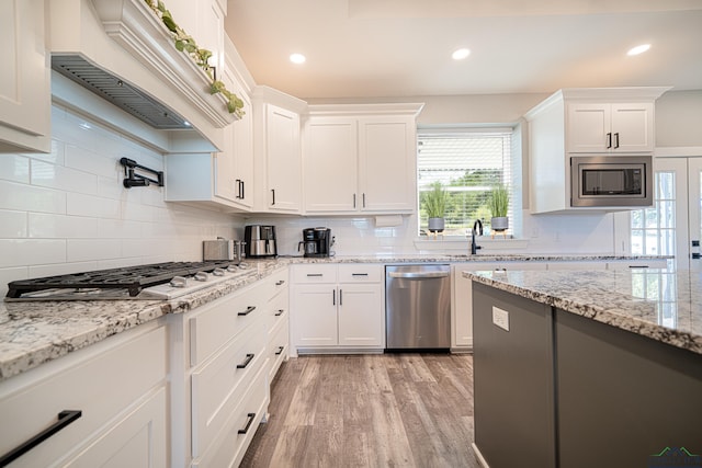 kitchen featuring white cabinets, stainless steel appliances, custom range hood, and light wood-type flooring